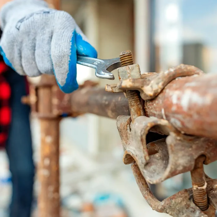 Worker tightening scaffolding clamp using wrench for secure installation on construction site
